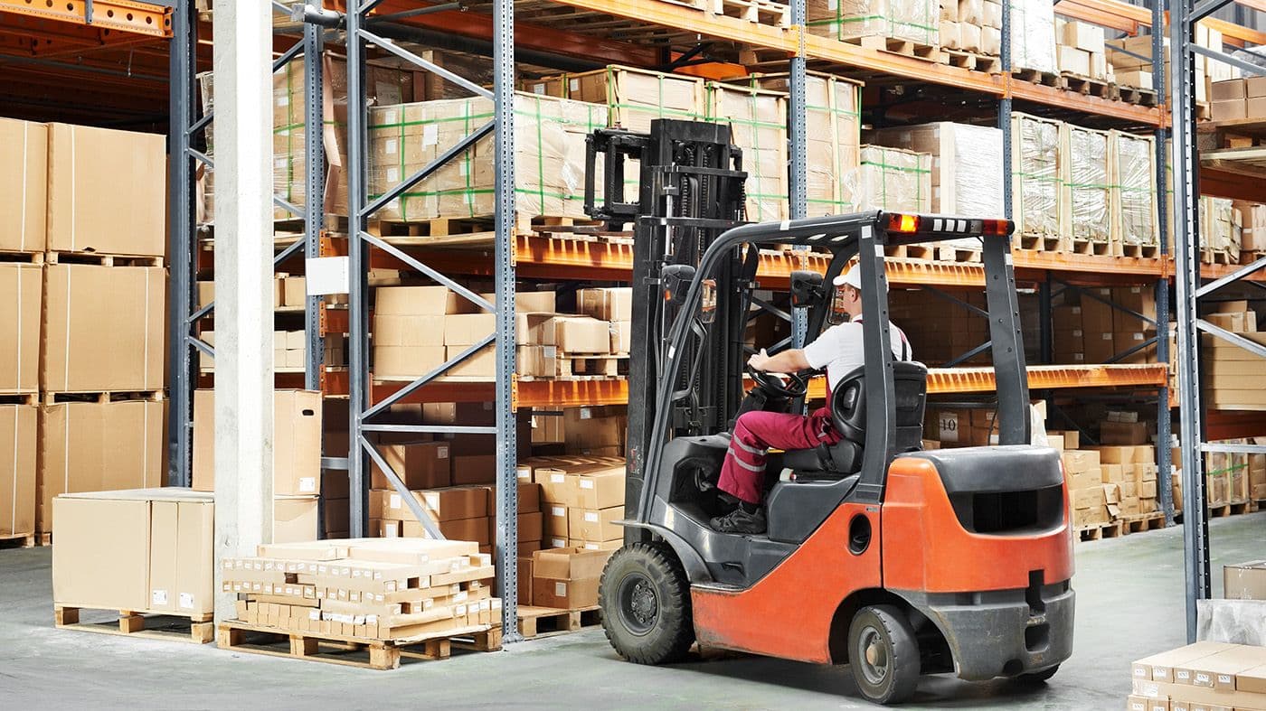 person in a warehouse standing near a forklift 